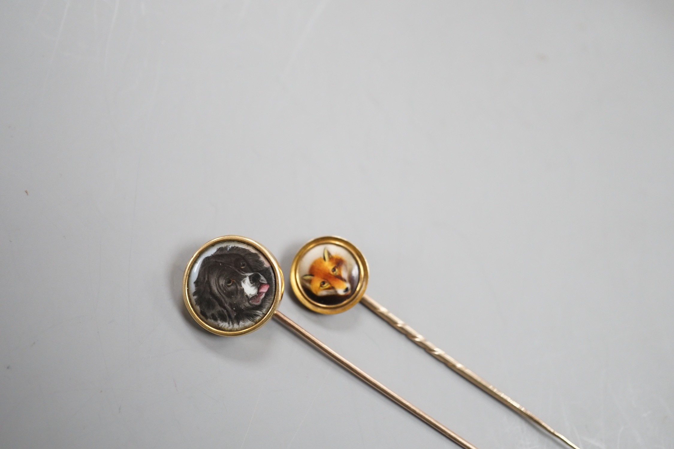 Two early 20th century yellow metal and enamel stick pins, both decorated with the head of a dog, largest, 70mm, gross weight 7.6 grams.